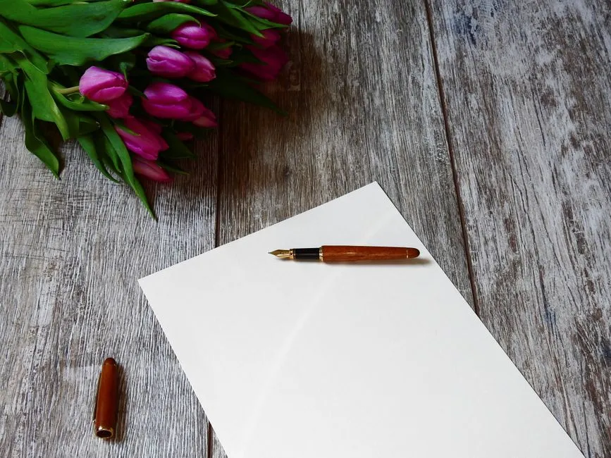 Ein leeres Blatt Papier und ein Füllfederhalter auf einem verwitterten Holztisch, mit einem Tulpenstrauß in der Ecke