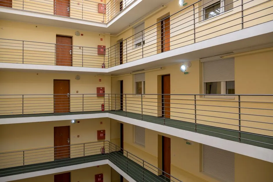 El patio interior de un edificio de apartamentos de varios pisos, visto desde una planta superior, mostrando varias filas de puertas numeradas a lo largo de pasillos abiertos con barandillas metálicas, sin personas visibles