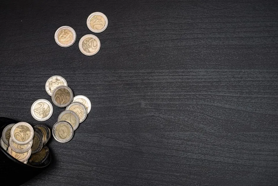 Zwei-Euro-Münzen fallen aus einer dunklen Tasse auf einen dunklen Holztisch