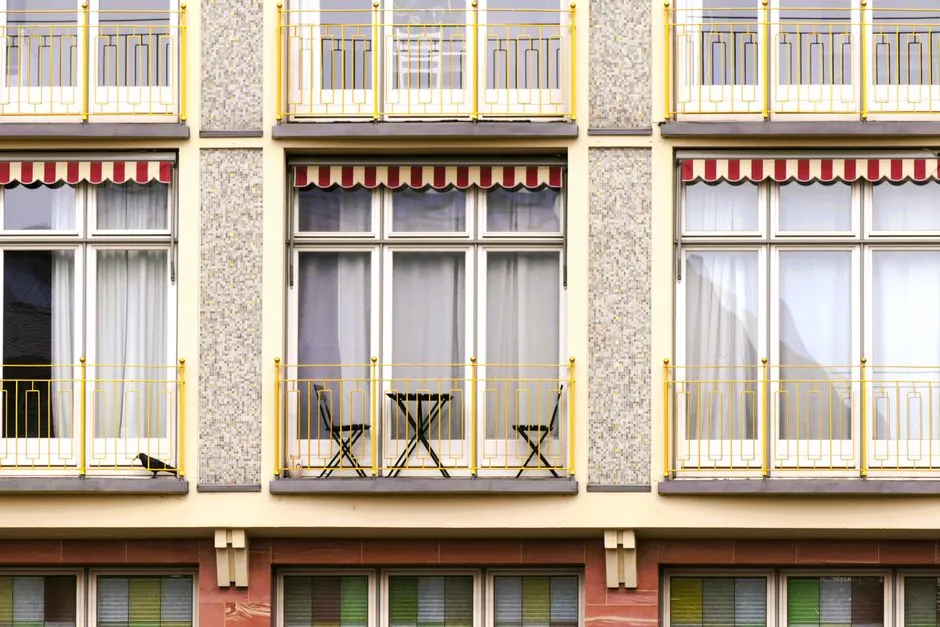 Balkone mit gestreiften Markisen, Bistrotischen und Stühlen an einer europäischen Wohnhausfassade, typisch für den Mietwohnungsbestand, um den sich Neuankömmlinge bewerben