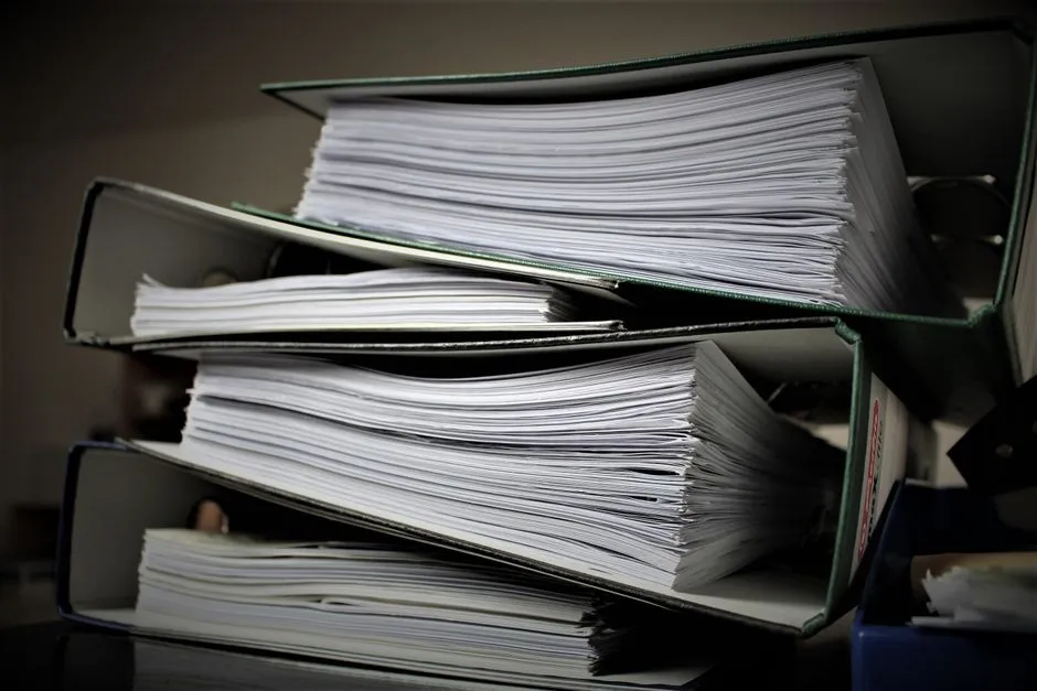Gestapelte Aktenordner voller Papier auf einem Schreibtisch, sinnbildlich für die wachsende Bewerbungsmappe eines ernsthaften Wohnungssuchenden