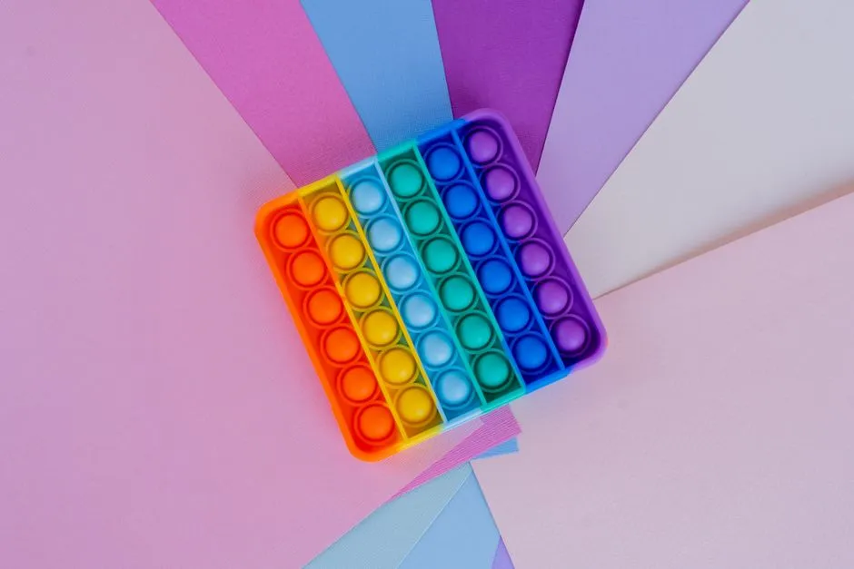 Un juguete sensorial de silicona con los colores del arcoíris apoyado sobre un fondo geométrico de tonos pastel, sin personas, sin texto legible
