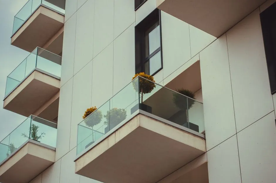 Schräge Ansicht einer modernen Wohnhausfassade mit glasbrüstungsverkleideten Balkonen, Topfpflanzen sichtbar, keine Menschen oder lesbarer Text