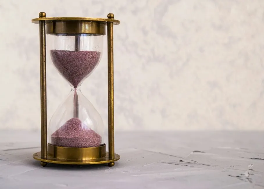 Eine Messing-Sanduhr mit rosa Sand, zur Hälfte durchgelaufen, auf einer strukturierten Steinfläche, keine Personen oder lesbarer Text sichtbar