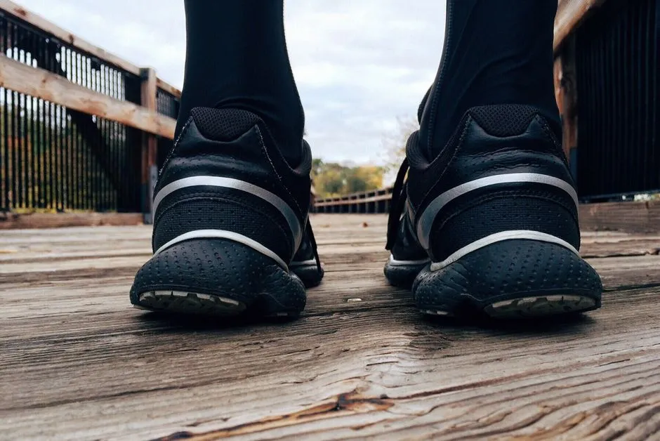 Nahaufnahme von Laufschuhen und Knoecheln von hinten gesehen auf einem hoelzernen Bohlenweg, eingerahmt von einem Gelaender, das in der Ferne zu Baeumen fuehrt