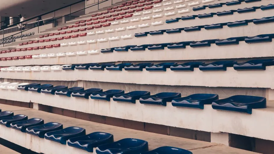 Reihen leerer roter, weißer und dunkelblauer Stadionsitze von oben gesehen, in einer gestuften Tribüne angeordnet