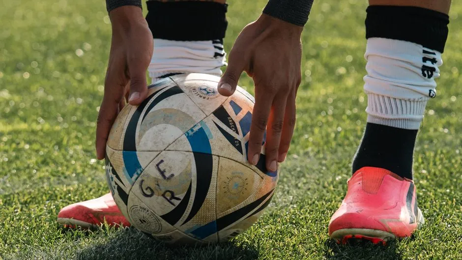 يدان تضعان كرة قدم على العشب، بجانب زوج من أحذية كرة القدم والجوارب، قبل ركلة