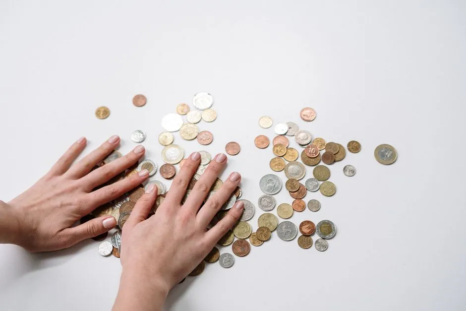 Two hands spread flat over a scattered pile of coins from different currencies on a plain surface