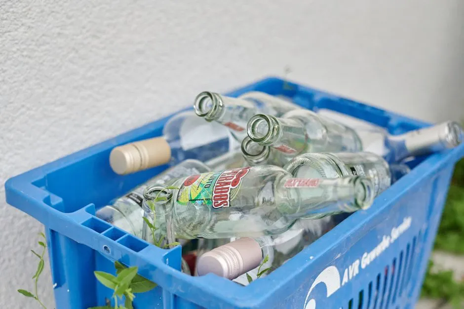 Yabancı etiketli boş cam şişelerin bir duvara yaslanmış mavi plastik içecek kasasında istiflenmesi