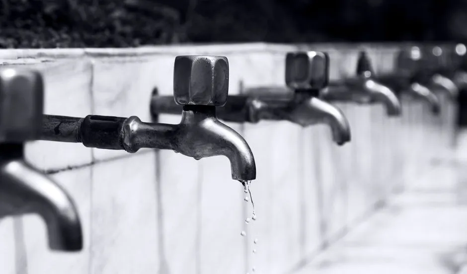 Una fila de grifos de agua metálicos con agua goteando de uno de ellos