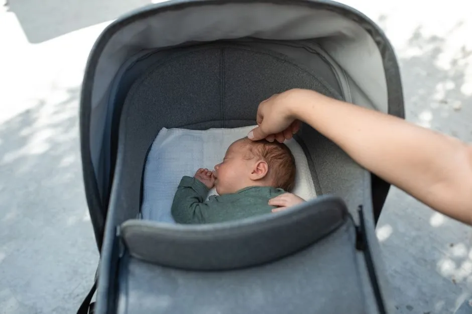 La mano de un padre o una madre descansa sobre la cabeza de un bebé dormido dentro de un cochecito