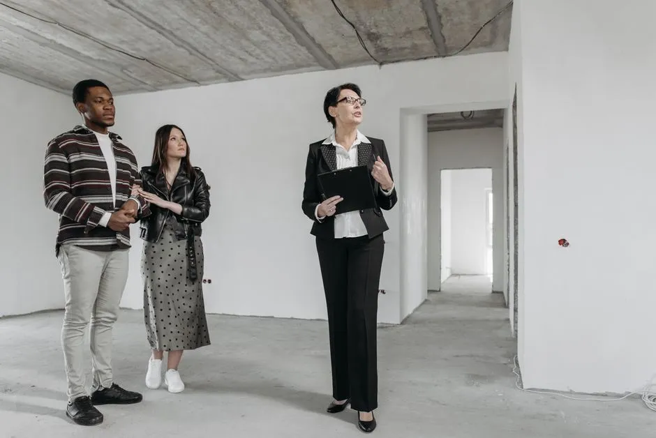 Elinde bir pano tutan bir emlakçının, çıplak betonlu, henüz tamamlanmamış bir daire içinde bir çiftle konuşurken çekilmiş fotoğrafı